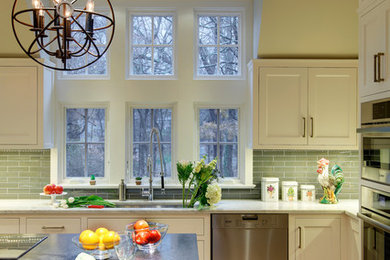 Large transitional u-shaped light wood floor enclosed kitchen photo in New York with a double-bowl sink, shaker cabinets, white cabinets, solid surface countertops, green backsplash, ceramic backsplash, stainless steel appliances and an island