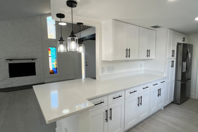 Mid-sized trendy galley vinyl floor and beige floor eat-in kitchen photo in Tampa with an undermount sink, raised-panel cabinets, white cabinets, quartz countertops, white backsplash, quartz backsplash, stainless steel appliances, a peninsula and white countertops