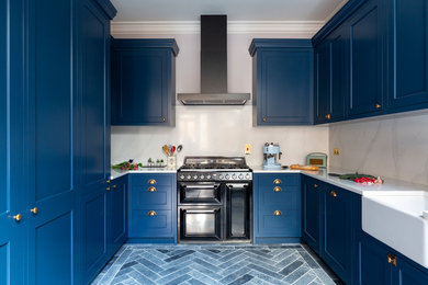 Mid-sized transitional u-shaped kitchen in London with a farmhouse sink, shaker cabinets, blue cabinets, marble benchtops, white splashback, marble splashback, black appliances, porcelain floors, blue floor and white benchtop.