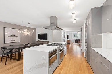 Example of a large minimalist medium tone wood floor eat-in kitchen design in New York with an undermount sink, flat-panel cabinets, gray cabinets, solid surface countertops, white backsplash, stainless steel appliances, an island and marble backsplash