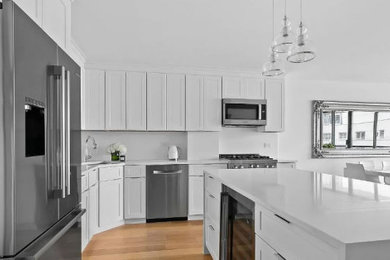 Eat-in kitchen - mid-sized contemporary galley medium tone wood floor eat-in kitchen idea in New York with an undermount sink, shaker cabinets, yellow cabinets, quartz countertops, white backsplash, ceramic backsplash, stainless steel appliances, an island and white countertops
