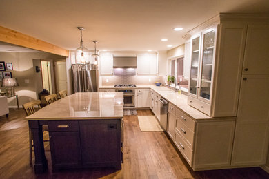 This is an example of a mid-sized traditional l-shaped open plan kitchen in Seattle with an undermount sink, recessed-panel cabinets, white cabinets, quartzite benchtops, white splashback, glass tile splashback, stainless steel appliances, medium hardwood floors, with island, brown floor and white benchtop.