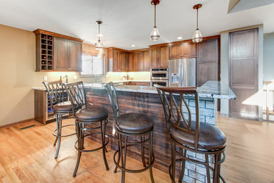 Photo of a large transitional u-shaped eat-in kitchen in Milwaukee with a farmhouse sink, flat-panel cabinets, brown cabinets, granite benchtops, stainless steel appliances, light hardwood floors, with island and yellow floor.