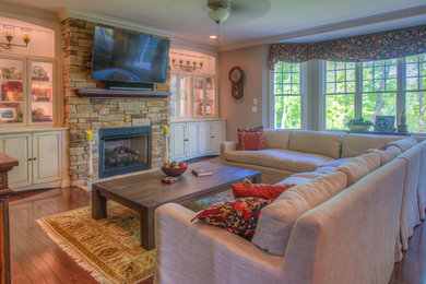 Photo of a large traditional open concept family room in Other with beige walls, medium hardwood floors, a standard fireplace, a stone fireplace surround, a wall-mounted tv and brown floor.
