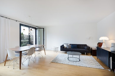 This is an example of a contemporary open concept living room in Paris with white walls, light hardwood floors and no fireplace.
