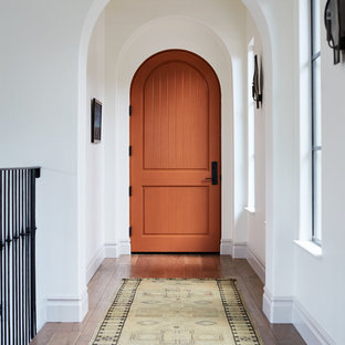 Esempio di una porta d'ingresso mediterranea di medie dimensioni con pareti bianche, pavimento in legno massello medio, una porta singola, una porta arancione e pavimento marrone