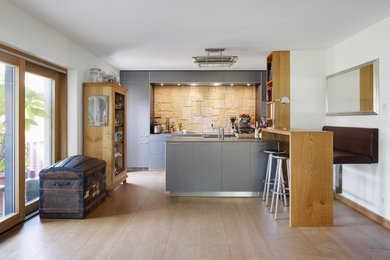 Offene, Zweizeilige Moderne Küche mit integriertem Waschbecken, flächenbündigen Schrankfronten, grauen Schränken, Mineralwerkstoff-Arbeitsplatte, Küchenrückwand in Beige, Küchengeräten aus Edelstahl, braunem Holzboden und Halbinsel in Berlin