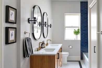 Example of a mid-sized transitional blue tile and ceramic tile porcelain tile, white floor and double-sink alcove shower design in Chicago with recessed-panel cabinets, medium tone wood cabinets, a one-piece toilet, white walls, an undermount sink, quartz countertops, a hinged shower door, white countertops and a floating vanity