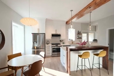 Example of a minimalist brown floor and exposed beam kitchen design in Toronto with shaker cabinets, white cabinets, white backsplash, stainless steel appliances, an island and white countertops
