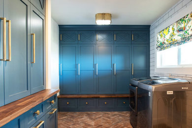 Inspiration for a small transitional brick floor utility room remodel in Denver with shaker cabinets, blue cabinets, wood countertops, white walls, a side-by-side washer/dryer and brown countertops