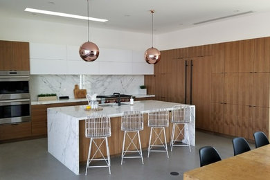 Large trendy l-shaped concrete floor and gray floor eat-in kitchen photo in Phoenix with an undermount sink, flat-panel cabinets, medium tone wood cabinets, marble countertops, white backsplash, stone slab backsplash, paneled appliances, an island and white countertops