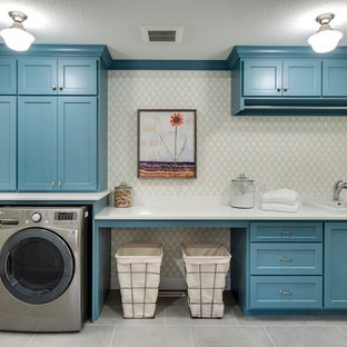 ミネアポリスの中サイズのトランジショナルスタイルのおしゃれな洗濯室 (ドロップインシンク、青いキャビネット、クオーツストーンカウンター、セラミックタイルの床、左右配置の洗濯機・乾燥機、落し込みパネル扉のキャビネット、グレーの床、白いキッチンカウンター、グレーの壁) の写真