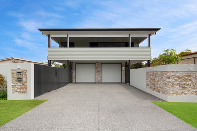 Photo of a mid-sized contemporary two-storey green duplex exterior in Brisbane with stone veneer, a flat roof, a metal roof, a white roof and board and batten siding.
