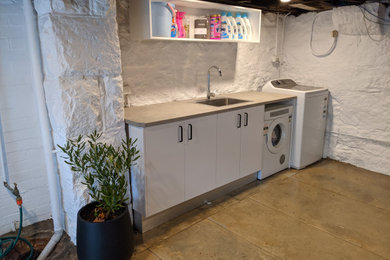 Design ideas for a mid-sized country galley dedicated laundry room in Sydney with a drop-in sink, white cabinets, concrete floors and brick walls.