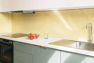 Ejemplo de cocina lineal actual de tamaño medio abierta con puertas de armario verdes, salpicadero amarillo, salpicadero de azulejos tipo metro y encimeras blancas