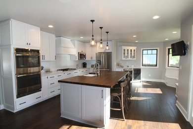 Design ideas for a mid-sized transitional l-shaped eat-in kitchen in Kansas City with a farmhouse sink, white cabinets, marble benchtops, white splashback, porcelain splashback, stainless steel appliances, dark hardwood floors, with island, shaker cabinets and brown floor.