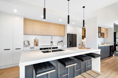 Inspiration for a large modern galley light wood floor and yellow floor open concept kitchen remodel in Auckland with a double-bowl sink, flat-panel cabinets, white cabinets, quartz countertops, white backsplash, subway tile backsplash, stainless steel appliances, an island and white countertops