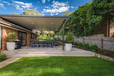 This is an example of a large contemporary backyard and ground level deck in Canberra - Queanbeyan with a pergola.