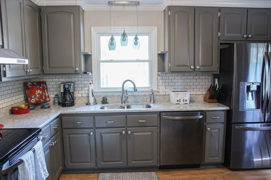 Inspiration for a contemporary l-shaped medium tone wood floor kitchen remodel in Raleigh with a double-bowl sink, raised-panel cabinets, gray cabinets, quartzite countertops, white backsplash, ceramic backsplash and stainless steel appliances