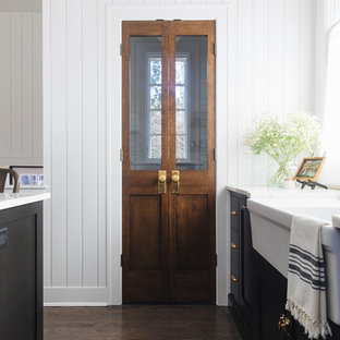 Inspiration for a mid-sized transitional l-shaped kitchen pantry in Chicago with a farmhouse sink, shaker cabinets, black cabinets, marble benchtops, white splashback, marble splashback, panelled appliances, medium hardwood floors, with island and brown floor.