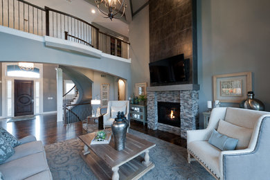Inspiration for a large transitional open concept living room in Kansas City with grey walls, dark hardwood floors, a standard fireplace, a stone fireplace surround, a wall-mounted tv and brown floor.