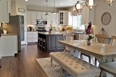 Example of a mid-sized transitional u-shaped vinyl floor and multicolored floor eat-in kitchen design in Other with a farmhouse sink, recessed-panel cabinets, white cabinets, granite countertops, metallic backsplash, metal backsplash, stainless steel appliances, an island and gray countertops