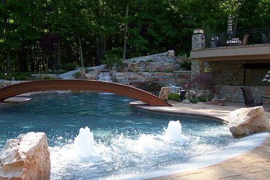 Photo of a large transitional backyard custom-shaped pool in Grand Rapids with stamped concrete and a water slide.