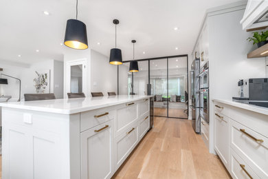 Example of a large trendy l-shaped light wood floor and brown floor open concept kitchen design in Toronto with a double-bowl sink, shaker cabinets, gray cabinets, quartz countertops, white backsplash, porcelain backsplash, stainless steel appliances, an island and white countertops