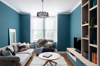Modelo de salón abierto de tamaño medio con paredes azules, suelo de madera en tonos medios, pared multimedia y suelo marrón