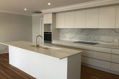 Photo of a mid-sized modern galley open plan kitchen in Other with an undermount sink, recessed-panel cabinets, white cabinets, solid surface benchtops, stone tile splashback, stainless steel appliances, vinyl floors, with island, brown floor and white benchtop.