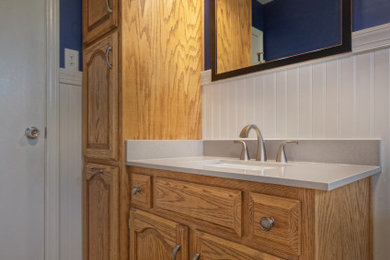 Bathroom - mid-sized vinyl floor, brown floor, single-sink and wall paneling bathroom idea with raised-panel cabinets, medium tone wood cabinets, blue walls, an undermount sink, quartzite countertops, gray countertops and a freestanding vanity
