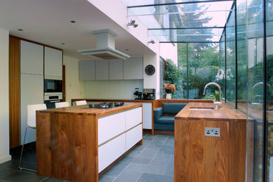 Mid-sized contemporary u-shaped kitchen in London with an undermount sink, flat-panel cabinets, white cabinets, wood benchtops, white splashback, glass sheet splashback, stainless steel appliances, ceramic floors and with island.