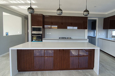 This is an example of an expansive modern kitchen pantry in Sydney with an undermount sink, flat-panel cabinets, brown cabinets, quartz benchtops, stainless steel appliances, multiple islands, white floor and white benchtop.