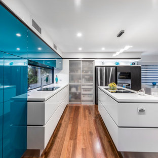 This is an example of a mid-sized contemporary l-shaped kitchen pantry in Brisbane with an undermount sink, flat-panel cabinets, turquoise cabinets, quartz benchtops, black appliances, medium hardwood floors and with island.