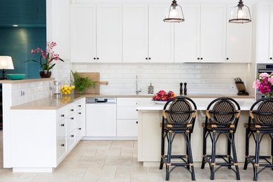 Photo of a beach style kitchen in Brisbane with shaker cabinets, white cabinets, white splashback, subway tile splashback, stainless steel appliances and with island.