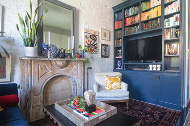 This is an example of an eclectic living room in New York with a library, white walls, dark hardwood floors and a built-in media wall.