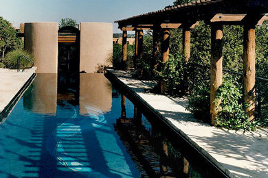 Inspiration for a mid-sized backyard rectangular infinity pool in Albuquerque with a pool house and concrete slab.