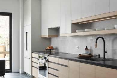 Example of a mid-sized trendy galley porcelain tile and black floor kitchen design in Toronto with a double-bowl sink, flat-panel cabinets, light wood cabinets, quartz countertops, gray backsplash, porcelain backsplash, stainless steel appliances, no island and black countertops