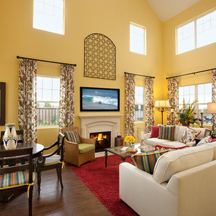 Geräumiges Mediterranes Wohnzimmer mit gelber Wandfarbe, dunklem Holzboden, Kamin, Kaminsims aus Stein und Wand-TV in Santa Barbara