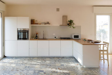 This is an example of a mid-sized contemporary l-shaped open plan kitchen in Other with a single-bowl sink, flat-panel cabinets, white cabinets, wood benchtops, grey splashback, panelled appliances, cement tiles, a peninsula, multi-coloured floor and brown benchtop.