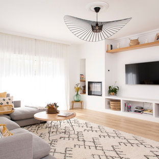 Modern inredning av ett stort allrum med öppen planlösning, med vita väggar, ljust trägolv, en standard öppen spis, en spiselkrans i metall, en väggmonterad TV och beiget golv