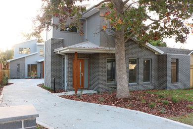 Photo of a mid-sized modern two-storey brick grey townhouse exterior in Melbourne with a gable roof and a metal roof.