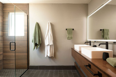 Modern inredning av ett stort brun brunt en-suite badrum, med skåp i mellenmörkt trä, beige väggar, ett fristående handfat, svart golv, dusch med gångjärnsdörr, våtrum, klinkergolv i porslin och träbänkskiva