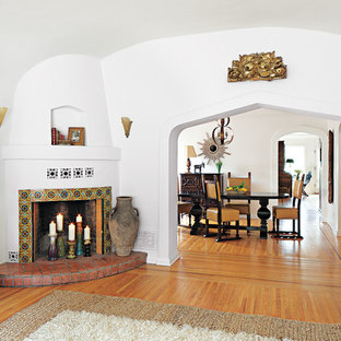 Modelo de salón mediterráneo con paredes blancas, suelo de madera en tonos medios, chimenea de esquina y marco de chimenea de baldosas y/o azulejos