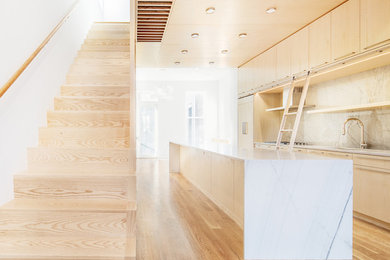 Open concept kitchen - modern galley open concept kitchen idea in New York with flat-panel cabinets, light wood cabinets, marble countertops, white backsplash, stone slab backsplash, paneled appliances and an island
