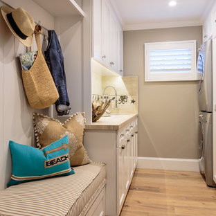 オレンジカウンティの大きいビーチスタイルのおしゃれな洗濯室 (シングルシンク、落し込みパネル扉のキャビネット、白いキャビネット、ライムストーンカウンター、グレーの壁、淡色無垢フローリング、上下配置の洗濯機・乾燥機) の写真