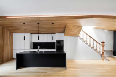 Example of a large trendy light wood floor kitchen design in Montreal with an undermount sink, flat-panel cabinets, quartzite countertops, black backsplash, stone slab backsplash, stainless steel appliances and an island