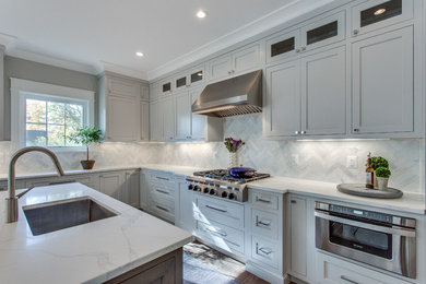 Photo of an expansive transitional u-shaped open plan kitchen in DC Metro with a single-bowl sink, shaker cabinets, grey cabinets, quartz benchtops, white splashback, marble splashback, stainless steel appliances, medium hardwood floors, with island and brown floor.