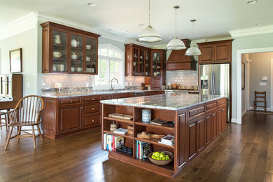 Photo of a mid-sized traditional l-shaped open plan kitchen in Nashville with an undermount sink, raised-panel cabinets, dark wood cabinets, granite benchtops, white splashback, ceramic splashback, stainless steel appliances, dark hardwood floors, with island and brown floor.