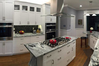 Inspiration for a large contemporary u-shaped light wood floor eat-in kitchen remodel in Other with a farmhouse sink, raised-panel cabinets, white cabinets, granite countertops, gray backsplash, stainless steel appliances and an island